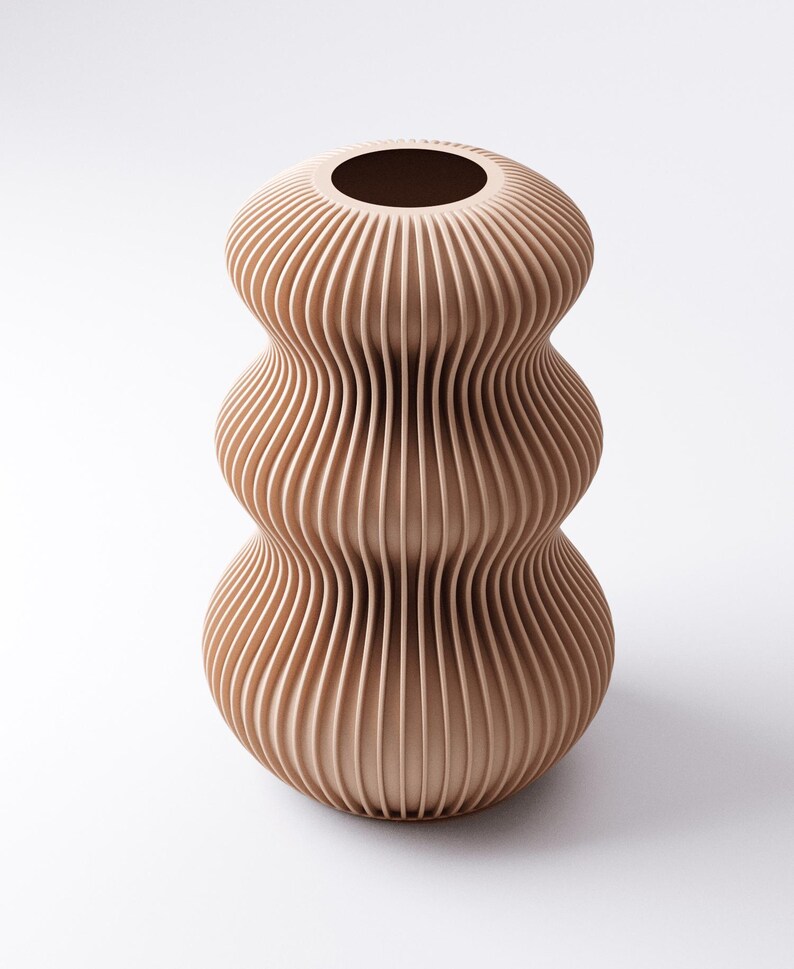 Peut inclure: Un vase beige &agrave; nervures verticales avec un design unique et superpos&eacute;. Le vase a une base large, une section centrale plus &eacute;troite et un sommet &eacute;vas&eacute; avec une ouverture circulaire. La texture nervur&eacute;e cr&eacute;e un jeu d'ombre et de lumi&egrave;re, am&eacute;liorant sa forme sculpturale.