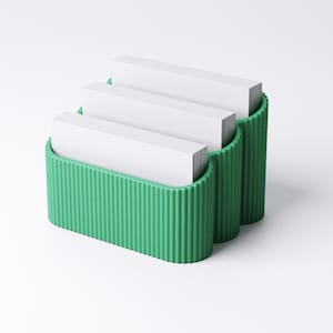 May include: A three-tiered, green business card holder with a ribbed design. Each tier holds a stack of white business cards. The holder is made of a solid material and is designed to sit on a desk or counter.