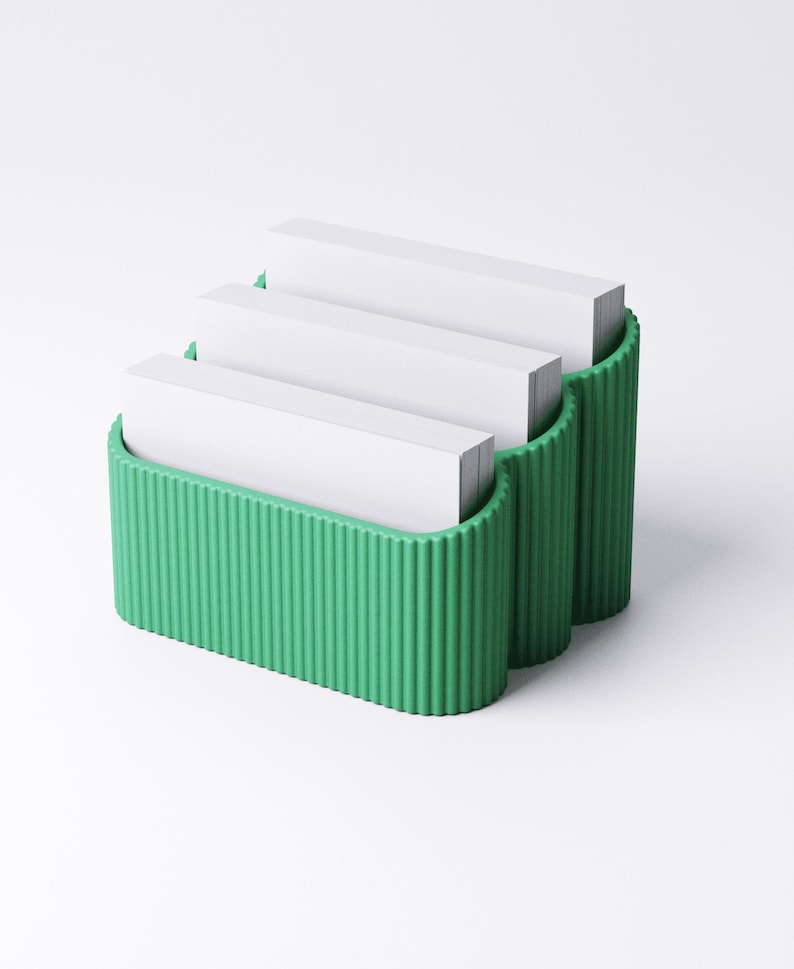 May include: A three-tiered, green business card holder with a ribbed design. Each tier holds a stack of white business cards. The holder is made of a solid material and is designed to sit on a desk or counter.