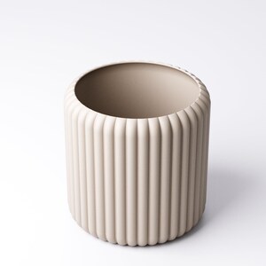 May include: A beige cylindrical vase with vertical ribbed detailing. The vase has a wide opening and a rounded base. The neutral color and minimalist design make it suitable for various home decor styles. The vase is made of ceramic.
