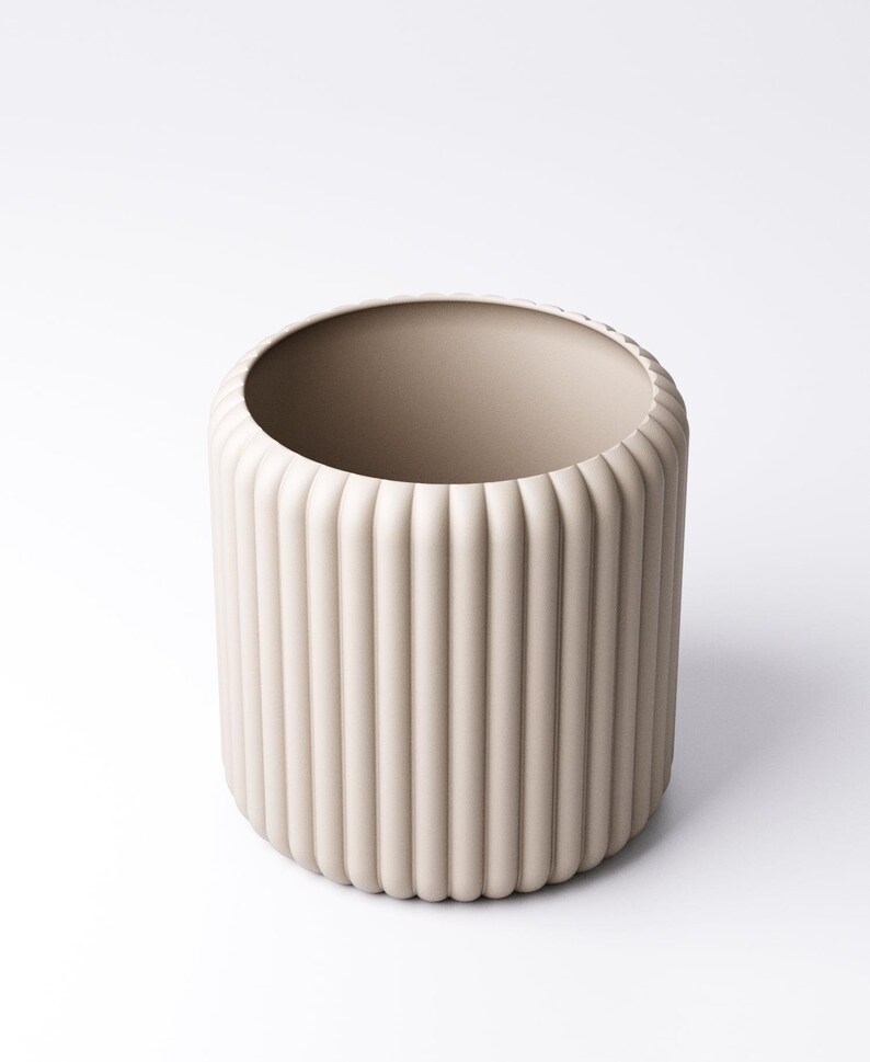 May include: A beige cylindrical vase with vertical ribbed detailing. The vase has a wide opening and a rounded base. The neutral color and minimalist design make it suitable for various home decor styles. The vase is made of ceramic.