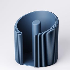 May include: A modern, blue paper towel holder. The holder has a cylindrical design with vertical ribbed detailing on the exterior and a central post. The open design allows for easy access to paper towels. The holder is made of a solid, matte material.