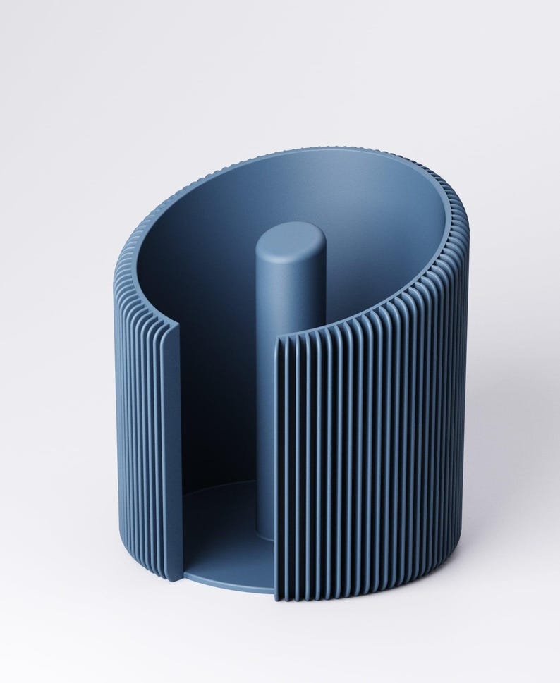 May include: A modern, blue paper towel holder. The holder has a cylindrical design with vertical ribbed detailing on the exterior and a central post. The open design allows for easy access to paper towels. The holder is made of a solid, matte material.