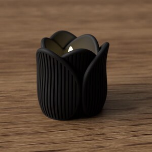 May include: A black tulip-shaped candle holder with a lit candle inside. The holder has vertical lines on the sides and is set on a wooden surface. The candle holder is approximately 3 inches tall.