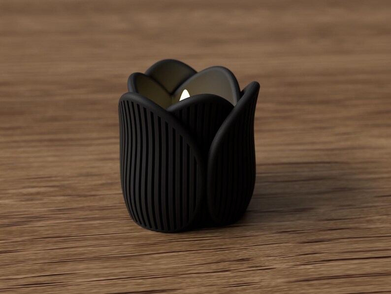 May include: A black tulip-shaped candle holder with a lit candle inside. The holder has vertical lines on the sides and is set on a wooden surface. The candle holder is approximately 3 inches tall.