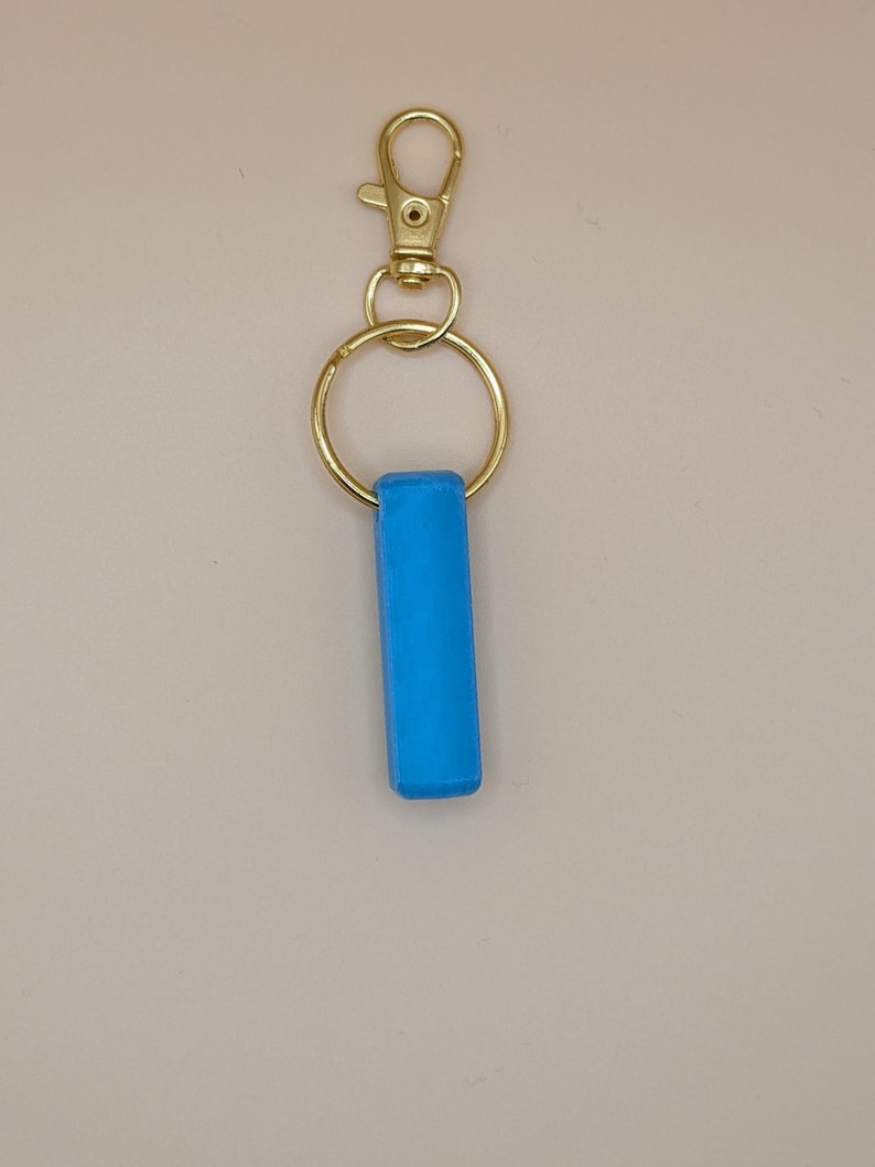 May include: A bright blue rectangular keychain charm attached to a gold-colored metal keyring and clasp. The charm is a solid, vibrant blue. The clasp is a lobster claw style.