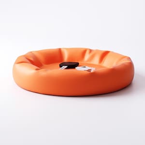 May include: An orange, circular tray with a raised edge. A black object and a white object are inside the tray. The tray is on a white background. The tray is likely used for organizing small items.