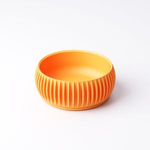 Pu&ograve; includere: Una ciotola arancione brillante con un esterno a coste e un interno liscio. La ciotola &egrave; rotonda e poggia su uno sfondo bianco. Il colore &egrave; un arancione brillante e solare.