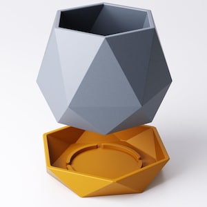 May include: A geometric, two-piece planter set. The upper planter is a faceted, gray polygon shape. The lower piece is a matching faceted polygon in a mustard yellow color, designed to catch water. The planter is designed to hold small plants.