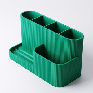 Pode incluir: Um organizador de secret&aacute;ria verde com v&aacute;rios compartimentos. O organizador tem uma base retangular com uma pequena bandeja e uma sec&ccedil;&atilde;o vertical curva com quatro ranhuras divididas. O exterior apresenta uma textura canelada.