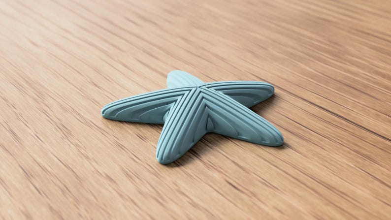 May include: A light blue starfish-shaped object with ribbed detailing. The five-pointed design is set against a wooden surface. The object appears to be made of a solid material.