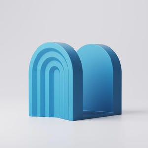 May include: A blue bookend with an arch design. The bookend has a solid, rectangular base and a curved top, with a series of nested arches on one side. The color is a solid, medium blue.