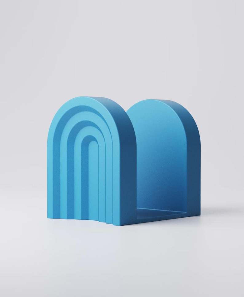 May include: A blue bookend with an arch design. The bookend has a solid, rectangular base and a curved top, with a series of nested arches on one side. The color is a solid, medium blue.