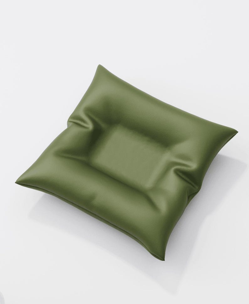 May include: Olive green square cushion with a slightly textured surface. The cushion has a rectangular indentation in the center. The pillow is angled, showing its shape and the way it catches the light.