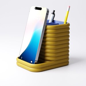 May include: A mustard yellow desk organizer with a ribbed design, holding a smartphone, a black pen, and a yellow pencil with a pink eraser. The organizer has a blue interior and sits on a white surface.