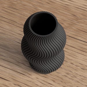May include: A black, decorative vase with a unique, wavy, textured design. The vase has a wide opening and a twisted, hourglass-like shape. The vase is sitting on a wooden surface.