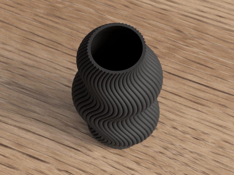 May include: A black, decorative vase with a unique, wavy, textured design. The vase has a wide opening and a twisted, hourglass-like shape. The vase is sitting on a wooden surface.