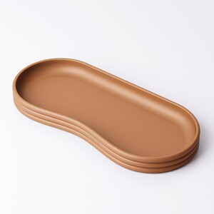 May include: A brown, oval-shaped serving tray with a raised edge and a ridged base. The tray is made of a solid material and has a smooth surface. The design is minimalist and modern, suitable for serving food or displaying items.