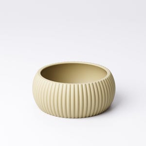 May include: A round, light beige ceramic bowl with vertical ribbed detailing. The bowl has a wide, open interior and a smooth, matte finish. The design is simple and modern, suitable for various uses.