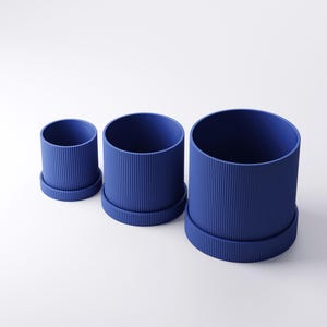 May include: Three blue cylindrical planters of varying sizes, each with a matching base. The planters have a ribbed texture on the exterior. The smallest planter is approximately 4 inches in diameter, while the largest is about 8 inches.
