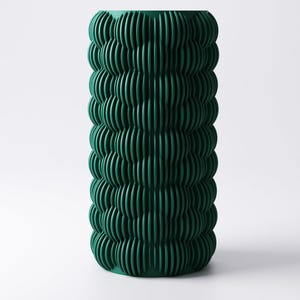May include: A tall, cylindrical vase in a deep teal green hue. The vase features a textured, ribbed design that wraps around the entire body. The vertical ridges create a wave-like pattern, adding visual interest to the decorative piece.