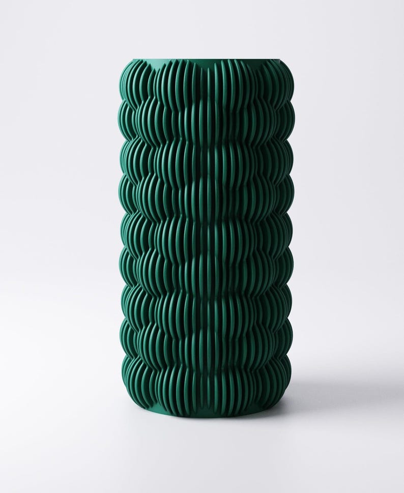 May include: A tall, cylindrical vase in a deep teal green hue. The vase features a textured, ribbed design that wraps around the entire body. The vertical ridges create a wave-like pattern, adding visual interest to the decorative piece.