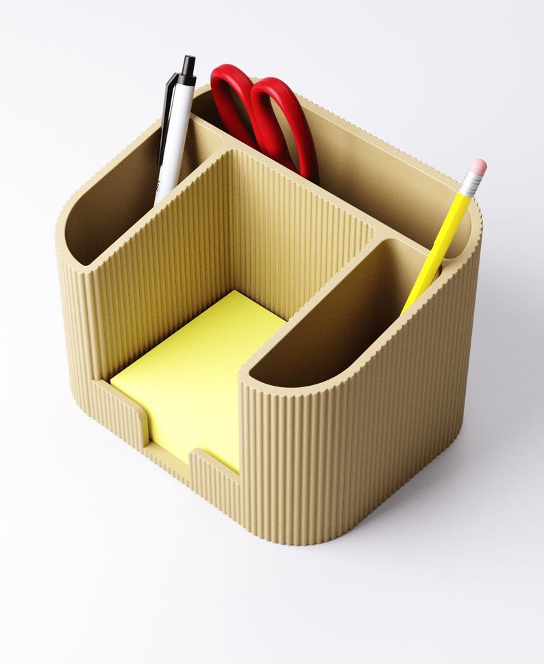 May include: A beige desk organizer with multiple compartments. It holds a yellow notepad, a white pen, red scissors, and a yellow pencil. The organizer has a ribbed texture and a curved design, suitable for office or home use.