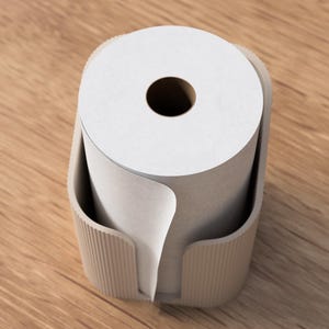 Op de afbeelding: Een beige papieren rolhouder met een witte papieren rol erin. De houder heeft een geribbelde textuur aan de zijkanten en een gebogen ontwerp om de papieren rol op zijn plaats te houden. De papieren rol heeft een donker gat in het midden.