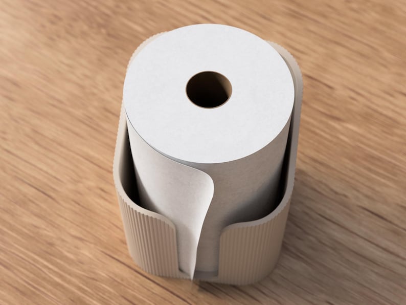 Op de afbeelding: Een beige papieren rolhouder met een witte papieren rol erin. De houder heeft een geribbelde textuur aan de zijkanten en een gebogen ontwerp om de papieren rol op zijn plaats te houden. De papieren rol heeft een donker gat in het midden.