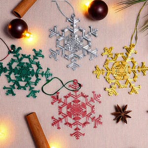May include: A collection of snowflake ornaments in silver, green, gold, and red. The ornaments are arranged with cinnamon sticks, star anise, and decorative lights, creating a festive holiday scene.