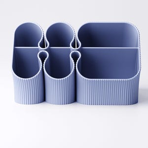 May include: A blue desk organizer with multiple compartments. The organizer has a ribbed texture and a rounded shape. It is designed to hold pens, pencils, and other office supplies. The organizer is made of plastic.