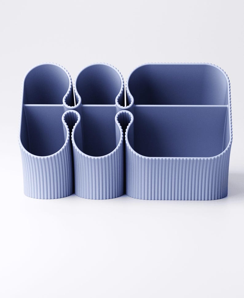 May include: A blue desk organizer with multiple compartments. The organizer has a ribbed texture and a rounded shape. It is designed to hold pens, pencils, and other office supplies. The organizer is made of plastic.