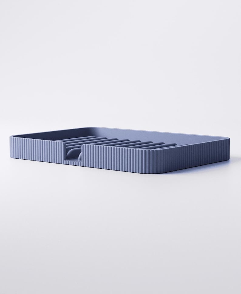 May include: A blue-grey rectangular dish rack with a ribbed exterior and interior slots for drying dishes. The rack has a small opening on one side for water drainage. The design is minimalist and modern.