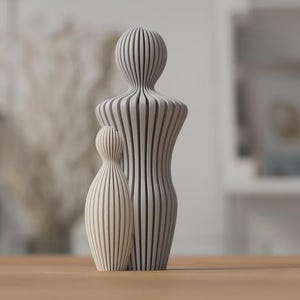 Puede incluir: Dos esculturas abstractas de madera, una grande y otra peque&ntilde;a, est&aacute;n una al lado de la otra. Las esculturas son de color claro con patrones de rayas verticales. La escultura m&aacute;s grande mide unos 25 cm de alto, y la m&aacute;s peque&ntilde;a unos 13 cm. Est&aacute;n colocadas sobre una superficie de madera.