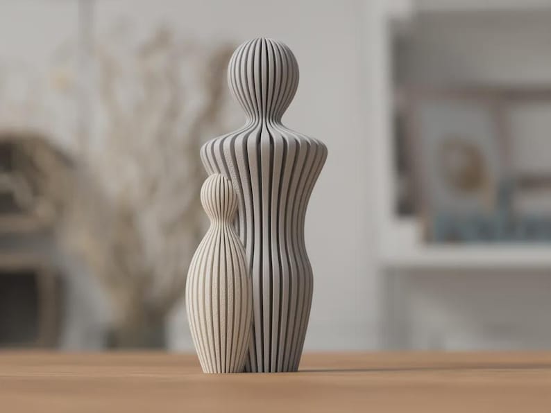 Puede incluir: Dos esculturas abstractas de madera, una grande y otra peque&ntilde;a, est&aacute;n una al lado de la otra. Las esculturas son de color claro con patrones de rayas verticales. La escultura m&aacute;s grande mide unos 25 cm de alto, y la m&aacute;s peque&ntilde;a unos 13 cm. Est&aacute;n colocadas sobre una superficie de madera.