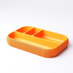 May include: A bright orange rectangular organizer with three compartments. The exterior features vertical ribbed detailing. The rounded corners and vibrant color give it a modern, minimalist aesthetic. Ideal for desk or drawer organization.