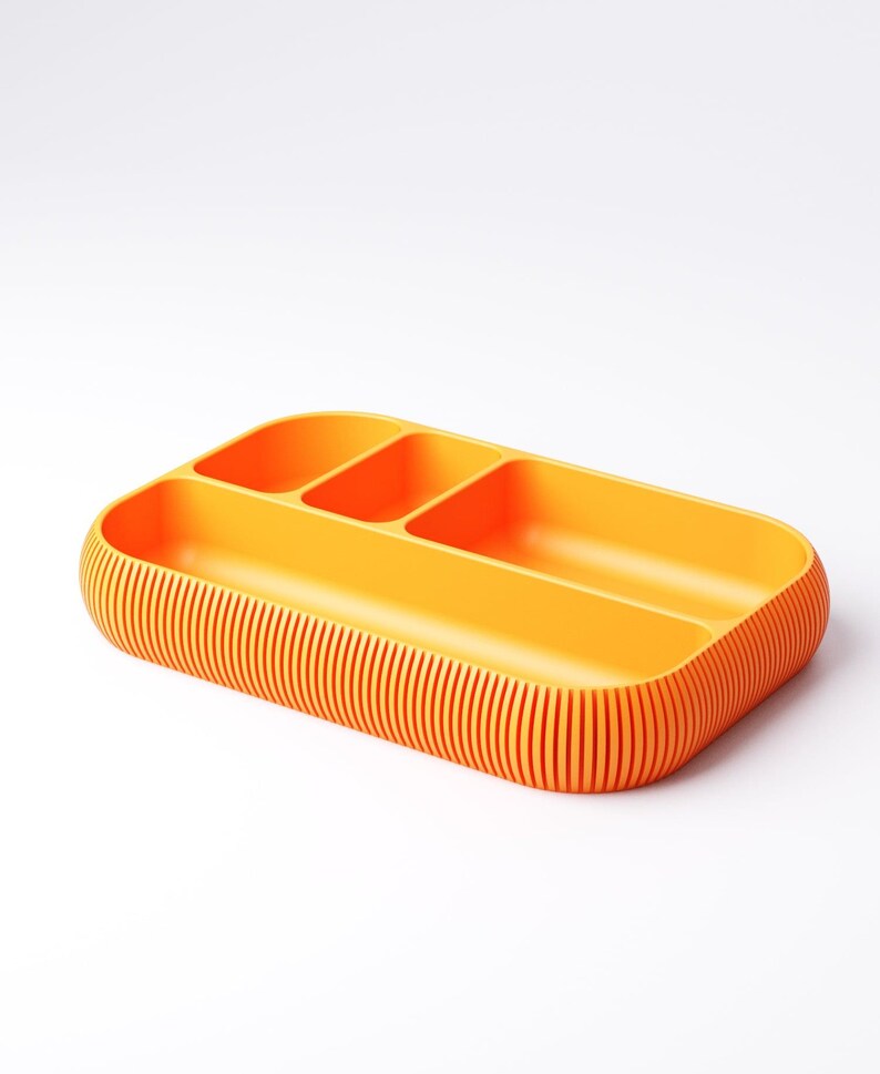 May include: A bright orange rectangular organizer with three compartments. The exterior features vertical ribbed detailing. The rounded corners and vibrant color give it a modern, minimalist aesthetic. Ideal for desk or drawer organization.