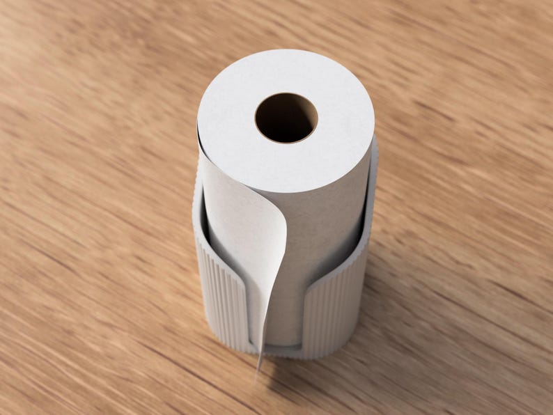 Op de afbeelding: Een witte papieren roldispenser met een rol wit papier. De dispenser is lichtgrijs van kleur en heeft een geribbeld ontwerp. Het papier is gedeeltelijk afgerold, wat de textuur van het papier laat zien. De dispenser staat op een houten oppervlak.