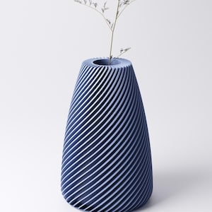 K&ouml;nnte beinhalten: Eine blaue Vase mit einem Spiraldesign. Die Vase hat eine breite &Ouml;ffnung und einen konischen K&ouml;rper. Ein kleiner, getrockneter Pflanzenstiel befindet sich im Inneren der Vase. Die Vase besteht aus einem festen Material und hat eine moderne &Auml;sthetik.