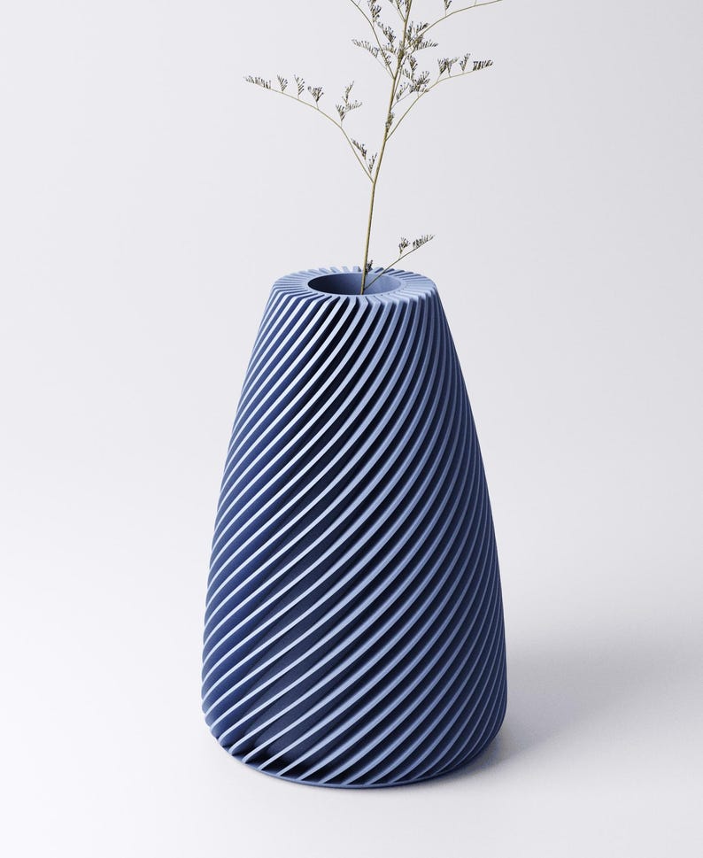 K&ouml;nnte beinhalten: Eine blaue Vase mit einem Spiraldesign. Die Vase hat eine breite &Ouml;ffnung und einen konischen K&ouml;rper. Ein kleiner, getrockneter Pflanzenstiel befindet sich im Inneren der Vase. Die Vase besteht aus einem festen Material und hat eine moderne &Auml;sthetik.