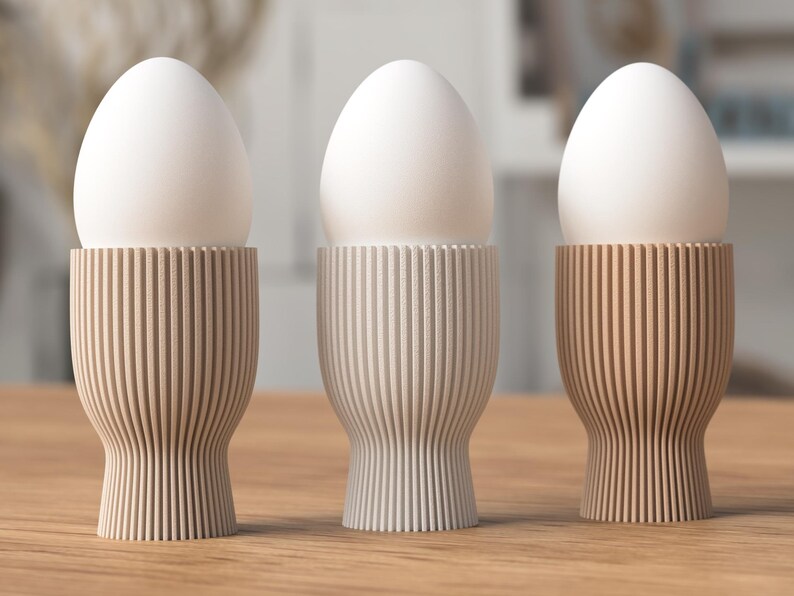 Pu&ograve; includere: Tre uova bianche poggiano in portauova decorativi. I portauova sono realizzati in un materiale di colore chiaro con scanalature verticali e ogni tazza ha una tonalit&agrave; beige unica. Le uova sono di un colore bianco brillante.
