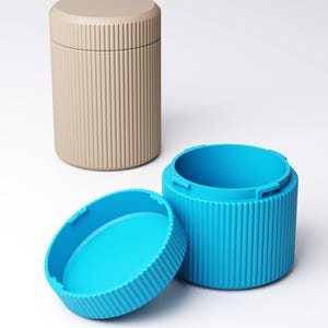 May include: A beige cylindrical container with a ribbed texture and a matching lid, positioned next to a bright blue cylindrical container with a matching ribbed texture and its lid placed separately in front of the open base.