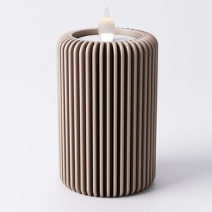 May include: A beige, cylindrical LED candle with a vertical ribbed design. The top features a recessed area with a flickering, flame-shaped light. The candle is designed to mimic the appearance of a real candle.