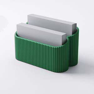 May include: A green business card holder with a ribbed exterior design. The holder is filled with two stacks of gray business cards. The holder has a curved shape and is made of a solid material.