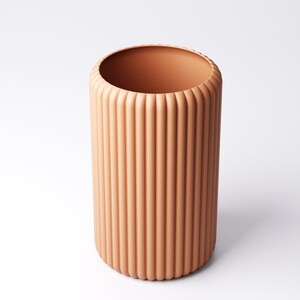 May include: A cylindrical, peach-colored vase with vertical, ridged detailing. The vase has a wide opening and a rounded base. The design is modern and minimalist, suitable for various decor styles. The vase is approximately 10 inches tall.