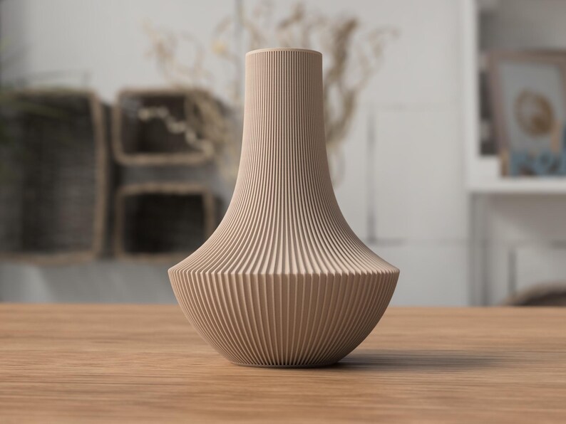 May include: A beige, ribbed vase with a wide base and a slender neck. The vase has a textured, vertical striped pattern. It is sitting on a wooden table, with a blurred background.