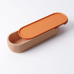 May include: An oval-shaped wooden box with a lid. The box is made of vertical wooden slats, and the lid is a solid orange color. The interior of the box is a light peach color. The lid is slightly ajar, revealing the interior.