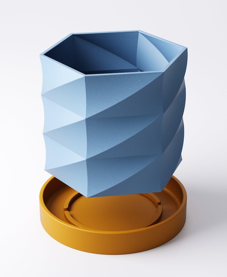 May include: A geometric blue vase with a textured surface, resting on a round, mustard-yellow base. The vase has a hexagonal top and a spiraling, faceted design. The base has a circular indentation.