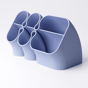 May include: A light blue desk organizer with a ribbed texture. The organizer has multiple compartments of varying sizes, with a curved design. The compartments are separated by white dividers. The overall design is modern and minimalist.
