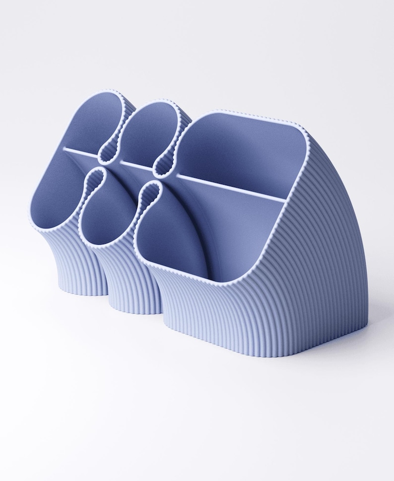 May include: A light blue desk organizer with a ribbed texture. The organizer has multiple compartments of varying sizes, with a curved design. The compartments are separated by white dividers. The overall design is modern and minimalist.